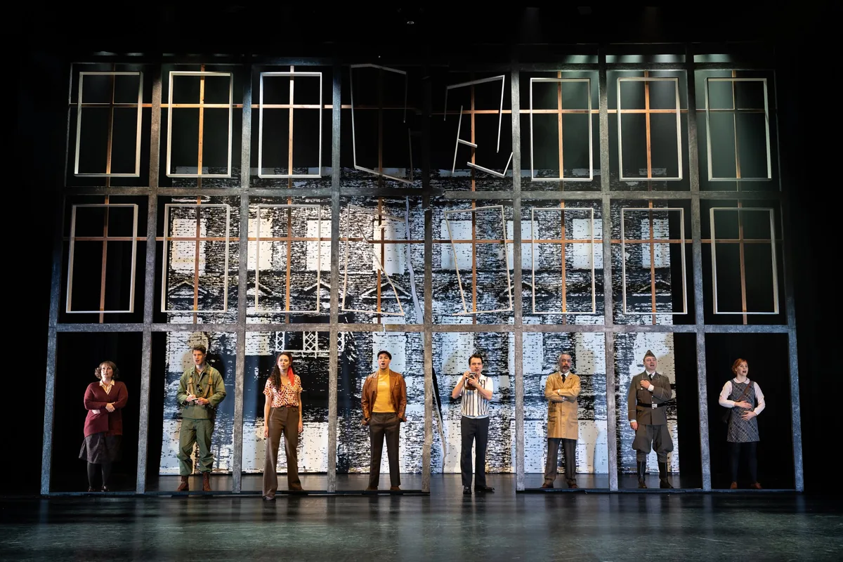 De volledige cast van Checkpoint Charlie op het toneel voor een wand van ramen