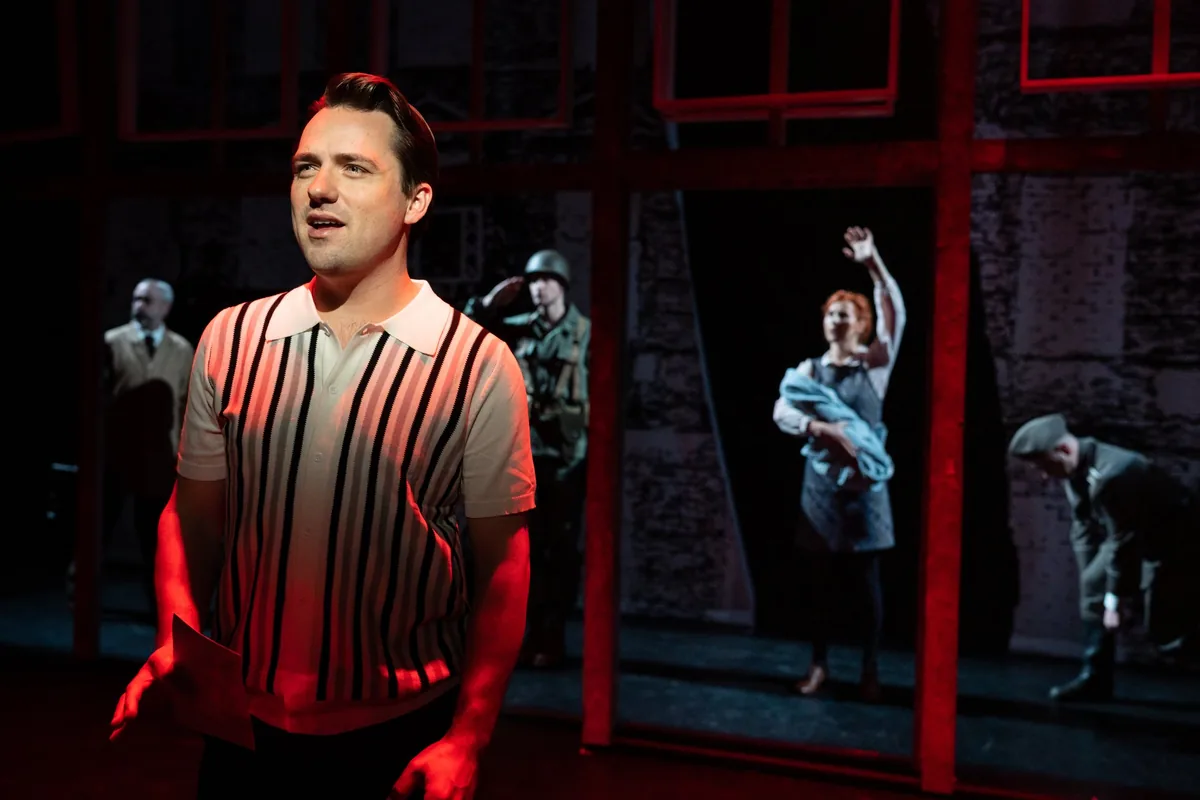 Scènefoto uit Checkpoint Charlie: een jonge man zingt voor de muur in rood licht