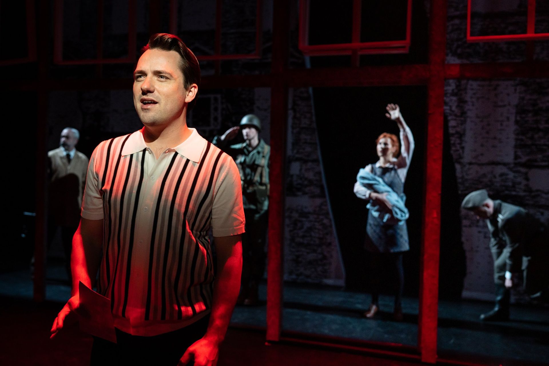 Een man in gestreept shirt zingt in rood licht, scène uit Checkpoint Charlie