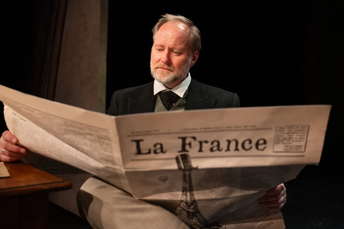 Scènefoto uit EIFFEL: een man leest de krant La France