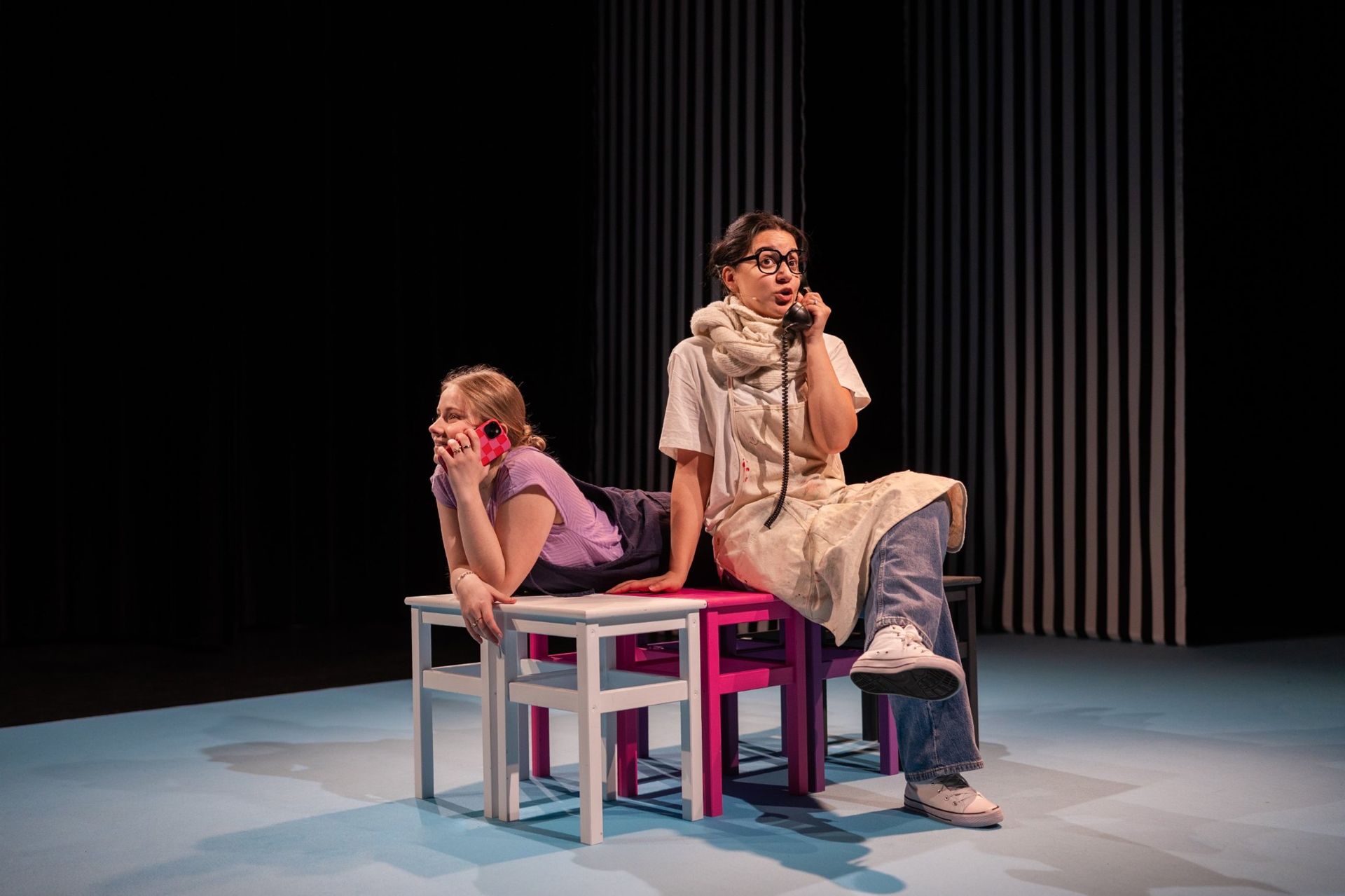 Sammy aan de telefoon, naast haar een vrouw met bril en een ouderwetse hoorn
