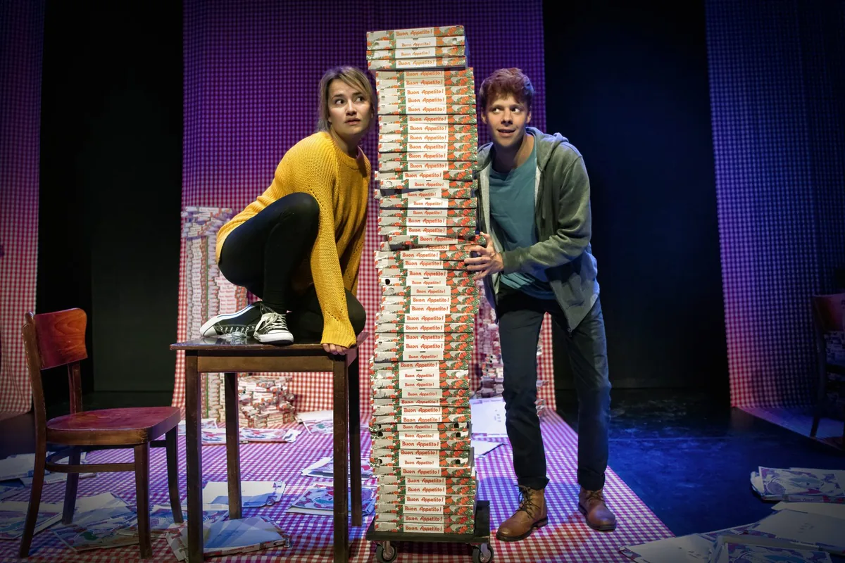 Scènefoto Romeo en Julia: Julia en Romeo naast een toren van pizzadozen